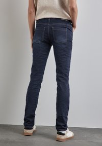 Jeans skinny-fit bleu foncé en denim, comportant cinq poches, un léger délavage et une taille mi-haute.