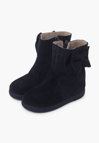 Botas de ante azul marino con un tubo corto, exterior texturizado y un lazo decorativo en el costado. Interior forrado con un suave material beige.