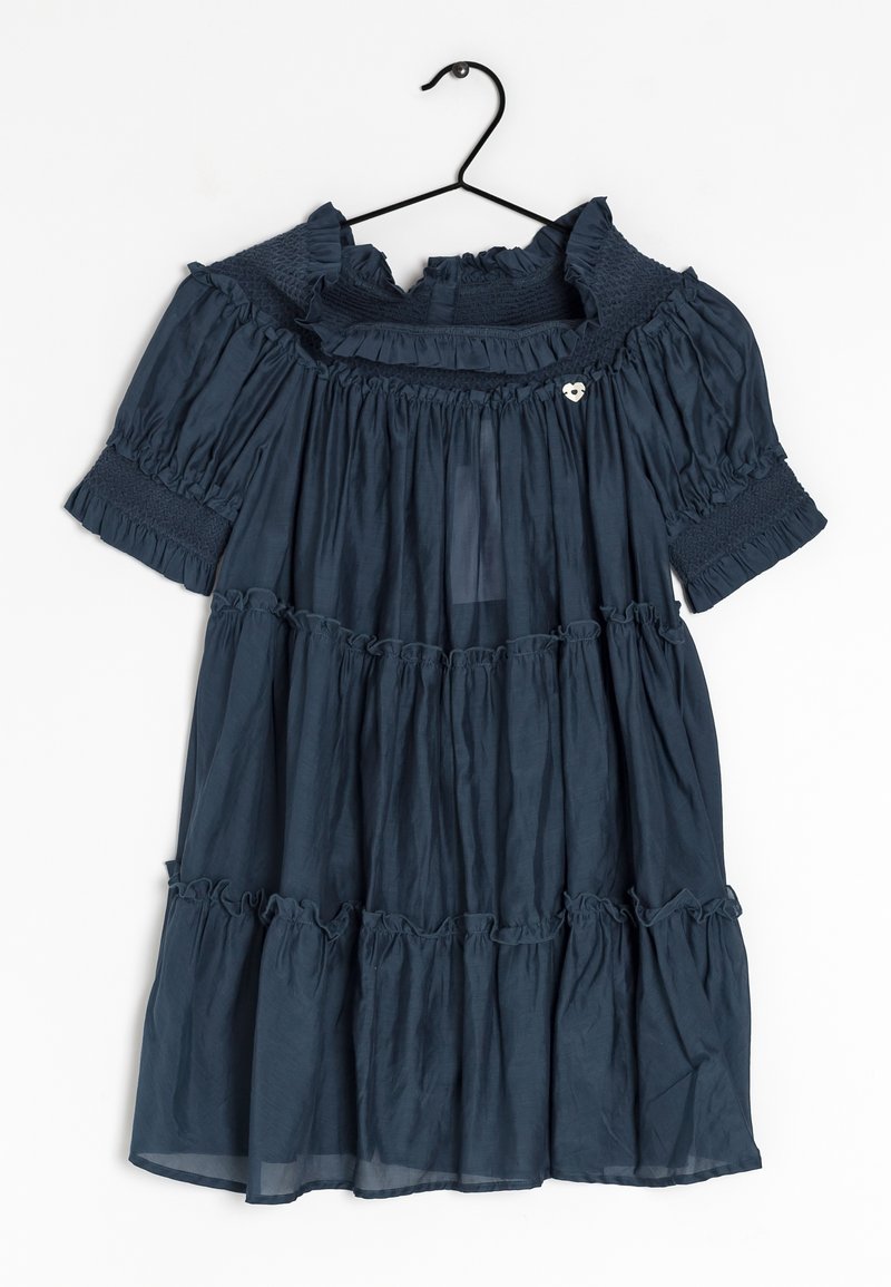 Abito blu navy a maniche corte con volant sovrapposti e dettagli smock appeso a una gruccia nera su sfondo bianco.