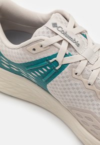 Lightweight athletic shoe featuring a beige mesh upper with teal synthetic accents, textured patterns, and a cushioned off-white sole.
