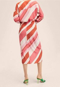 Abito lungo con strisce diagonali rosa, rosse e bianche. Realizzato in un tessuto leggero. Abbinato a sandali con tacco verde.