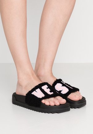 Sorte slides-sandaler med en blød overdel, der har bogstaverne "VE" i pink. Sålens underside er tekstureret for at give godt greb, og de er designet til afslappet brug.