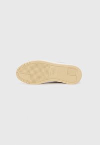 Baskets blanches avec une semelle en caoutchouc texturée de couleur beige clair. Bout arrondi, dessus en cuir lisse, et design minimaliste. Logo présent sur la semelle.