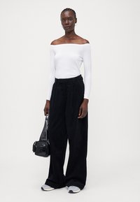 Hvit off-the-shoulder langermet topp kombinert med løse svarte cordbukser. Modellen bærer en liten svart håndveske og har på seg grå joggesko.