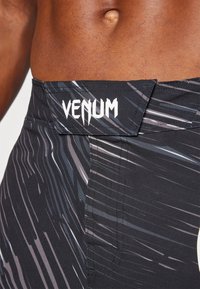 Črne trening hlače s mat površino, dinamičnimi sivo-belimi progami in izstopajočim logotipom "VENUM" na pasu.