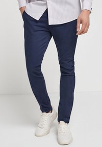Morske slim-fit hlače iz gladkega blaga, z višjim pasom in stranskimi žepi, v kombinaciji z belimi športnimi copati.