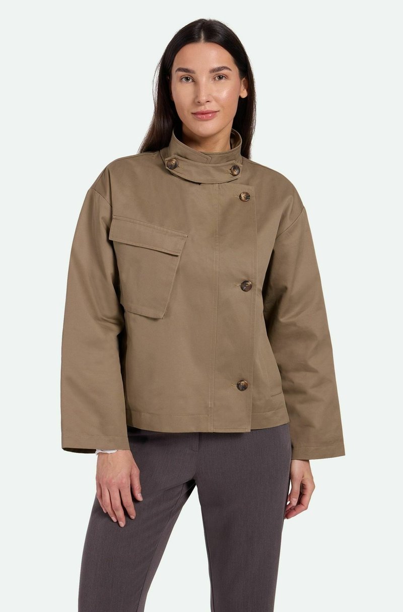 Chaqueta corta color arena con cuello alto, cierre de cuatro botones y un bolsillo parche en la parte delantera. Textura suave y un corte relajado.