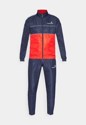 Tracksuit made of smooth, lightweight fabric. The jacket features a navy top and red bottom with white horizontal stripes. Pants are solid navy.