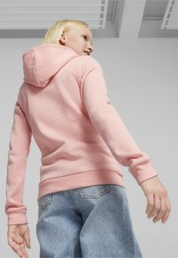 Sudadera rosa hecha de tela suave, con capucha ajustable y puños acanalados. Combinada con jeans de denim azul claro, que presentan un corte relajado.