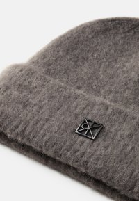 Szary, dzianinowy beanie o miękkim, teksturowanym wykończeniu. Posiada czarną łatkę z geometrycznym logo po boku. Żebrowany design dodaje wizualnego zainteresowania.
