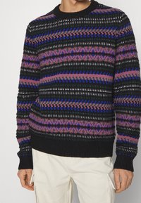 Neulepaita, jonka musta perusväri on varustettu vaakasuorilla raitoja vaaleanpunaisessa, purppurassa ja sinisessä. Ribbed hihansuut ja helma, joissa on monimutkaisia kuvioita.