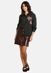 Black button-up shirt with pink floral embroidery, paired with a glossy burgundy mini skirt. Model wears dark sneakers with white laces.