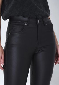 Černé kalhoty z umělé kůže s hladkým a lesklým povrchem. Mají vysoký pas, pět kapes a stříbrné kovové detaily.