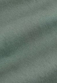 Gros plan sur un tissu doux vert clair avec une fine texture côtelée diagonale et des plis doux créant des ombres subtiles.
