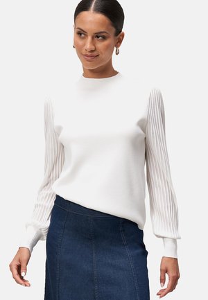 White sweater with ribbed long sleeves and fitted body; paired with a dark denim skirt. The texture is smooth with a slight sheen.