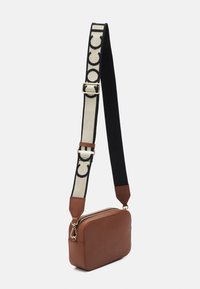 Ruskea suorakulmainen olkalaukku, jossa on teksturoidusta nahasta valmistettu pinta, kultainen vetoketju ja säädettävä musta-beige olkahihna, jossa on osittainen logo.