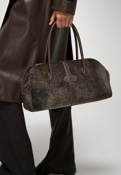 Borsa a mano in feltro marrone con dettagli in pelle, forma arrotondata e doppi manici. Presenta una toppa con logo e una texture a contrasto.