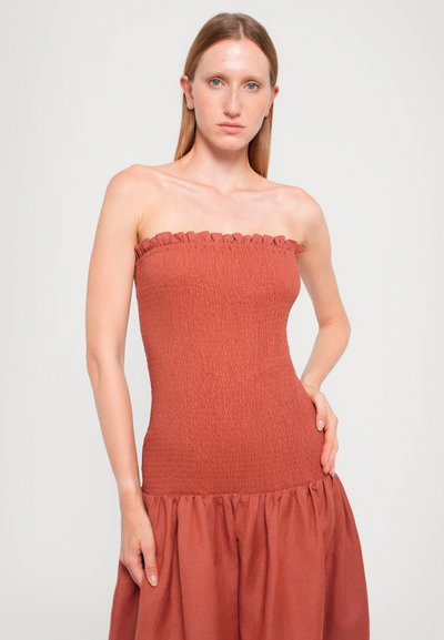 Strapless, rust-colored dress with smocked bodice and ruffled top. Flared skirt with gathered texture at the hem. Smooth fabric finish.