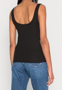 Svart ribbad linne med scoop back och breda axelband, kombinerat med ljusblå denimjeans som visar en avslappnad passform.