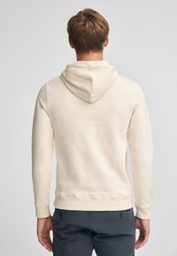 Felpa beige con cappuccio, maniche lunghe, polsini a coste e tasca a marsupio. Tessuto morbido con una texture liscia, vista posteriore mostrata.