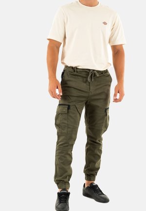 Pantalons cargo vert olive avec des poignets élastiques, de multiples poches et une taille à cordon, associés à un t-shirt casual beige clair.