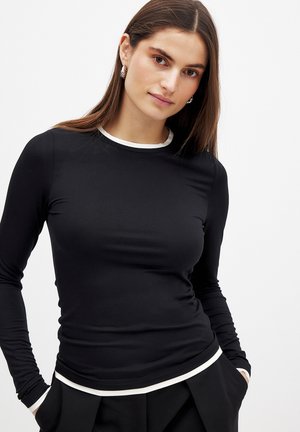 Maglietta nera a maniche lunghe con scollatura rotonda. Presenta un bordo bianco lungo il colletto. Realizzata in un materiale liscio ed elastico.