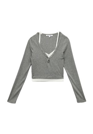 Top gris recortado de manga larga con escote en V profundo, con ribetes blancos y botones decorativos a lo largo del escote. Textura suave de punto.