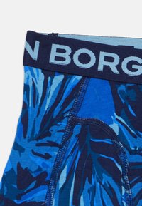 Sinine mustriga bokserid, millel on tumesinine vöökoht, millel on kergelt sinine tekst "BORG". Kangas näitab erinevate siniste toonide ja tekstuuride segu.