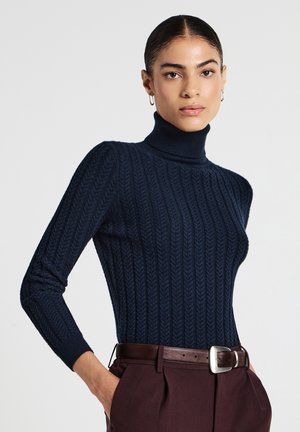 Maglione a collo alto navy a coste con un motivo texturizzato, dotato di maniche lunghe, aderente al corpo, abbinato a pantaloni marroni a vita alta.
