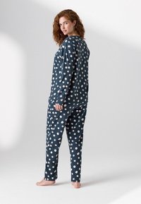 Marineblå pyjamas lavet af blødt stof med hvide prikker, der har en langærmet top og bukser med elastisk talje.