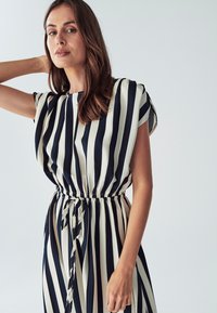 Raidallinen mekko, jossa on merinetty sinivalkoiset pystysuorat raidat, lyhyet hihat, elastinen vyötärö, jossa on nauha, sekä sileä kangas.