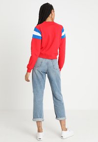 Felpa rossa con strisce blu e bianche sulle spalle, polsini e orlo a coste; abbinata a jeans azzurri arrotolati e sneaker bianche.
