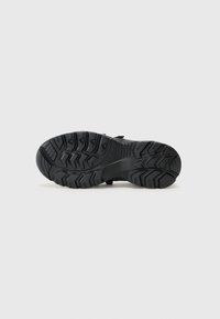 Suela de zapato negra y resistente con surcos profundos, que proporcionan agarre. Presenta una forma curva, hecha de goma duradera con patrones de tracción pronunciados.