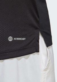 Camiseta deportiva negra AEROREADY con una superficie texturizada, que presenta un logotipo blanco. El dobladillo de la camiseta se complementa con pantalones cortos blancos.
