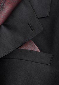 Poche d'une veste noire avec un mouchoir de poche rose à motif partiellement visible sous le revers.
