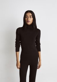 Juodas megztas turtleneko jumpsuit'as su ilgomis rankovėmis, prigludęs dizainas ir griovelis tekstūra. Minkšta medžiaga be matomų raštų ar akcentų.