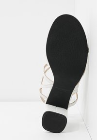Sandale blanche à lanières avec semelle noire texturée et talon carré bas, taille 37, positionnée debout sur un fond blanc.