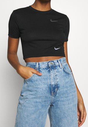 Osoba nosząca czarną krótką koszulkę Nike z dwoma białymi logo Swoosh oraz jasnoniebieskie dżinsy z wysokim stanem, jedna ręka w kieszeni.
