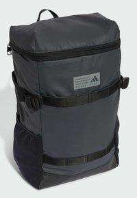 Dunkelgrauer Rucksack mit strukturierter Oberseite, Reißverschluss, Seitentaschen und verstellbaren Trägern. Verfügt über ein Logetikett und strukturierte Akzente.
