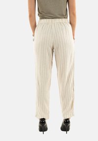 Lichtbeige linnenbroek met verticale strepen, elastische tailleband, zijzakken en een taps toelopend ontwerp, gedragen met zwarte hoge hakken.