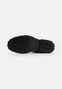 Suela de zapato de goma negra con un patrón de tracción robusto y un marcado detalle de surcos, diseñada para ofrecer agarre y durabilidad.