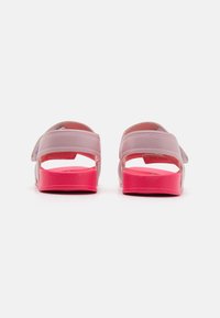 Roze en lavendelkleurige sandalen met verstelbare banden, open achterkant en roze gestructureerde zolen, die een speels kleurcontrast benadrukken.