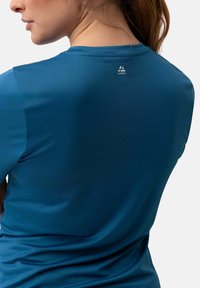 Blaues Sportshirt aus strukturiertem, atmungsaktivem Material. Hat einen runden Ausschnitt und ein kleines Logo nahe der Rückenschulter.