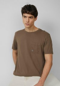 Bruine korte mouwen t-shirt van katoen, met een zak op de linkerborst met een klein logo, ronde halslijn en een relaxte pasvorm.