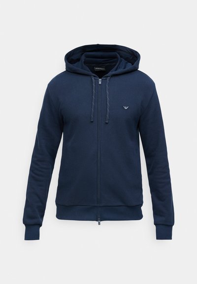 Navy zip-up dukserica s kapuljačom izrađena od teksturirane tkanine, s vezicom za kapuljaču, rebrastim manžetama i malim logom na lijevoj strani prsiju.