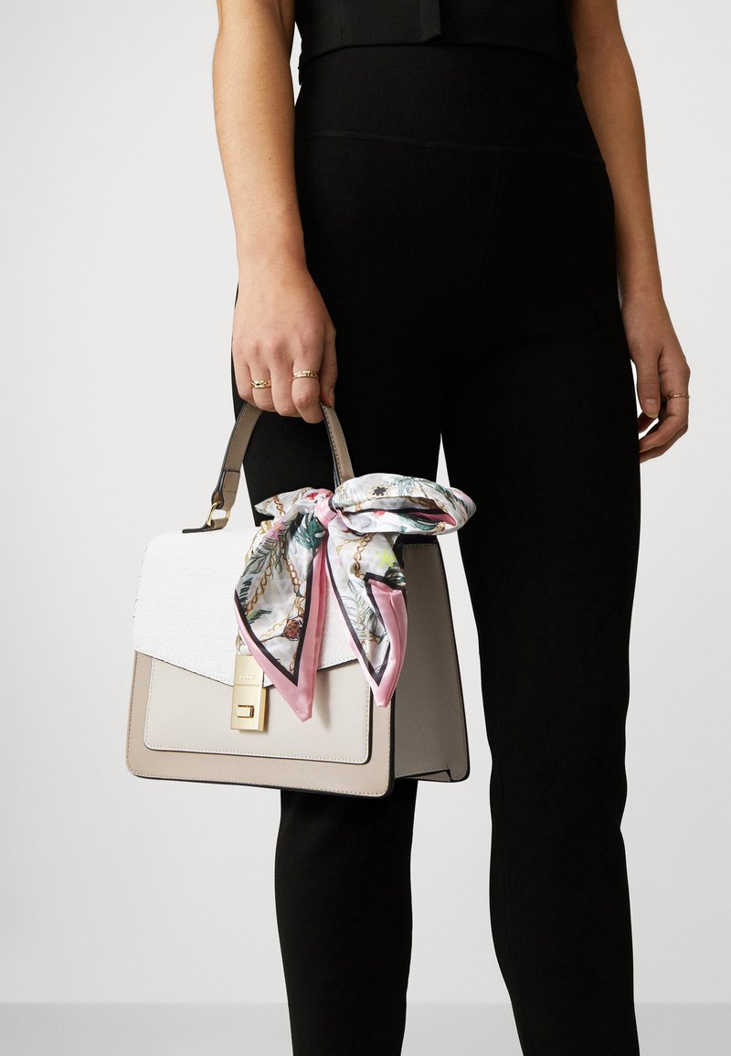 Sac à main beige avec un rabat texturé blanc, des accessoires en or, et une écharpe en soie à motif floral nouée sur la poignée. Matériau lisse, forme structurée.