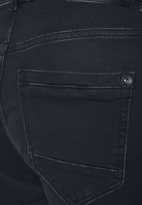 Czarne dżinsy o gładkiej fakturze, z jedną tylną kieszenią, subtelnym guzikiem z logo oraz kontrastowymi detalami w szwie.