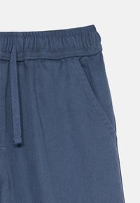 Blue elastic waistband pants with a drawstring and side pocket, made from textured, ribbed fabric.