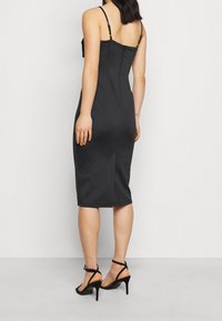 Svart figurnära klänning med justerbara band, knälång, slät textur och dragkedja bak. Matchad med svarta sandaletter med remmar.