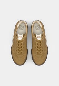 Καφέ σουέτ αθλητικά παπούτσια με λευκές λεπτομέρειες, στρογγυλεμένες μύτες και επίπεδα κορδόνια. Διαθέτουν υφή στην επιφάνεια και λογότυπο στην γλώσσα.